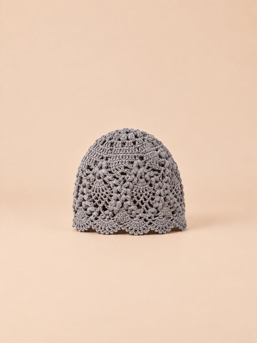 Gorro de verano gris de encaje floral con flores caladas y borde ondulado, fotografiado de frente
