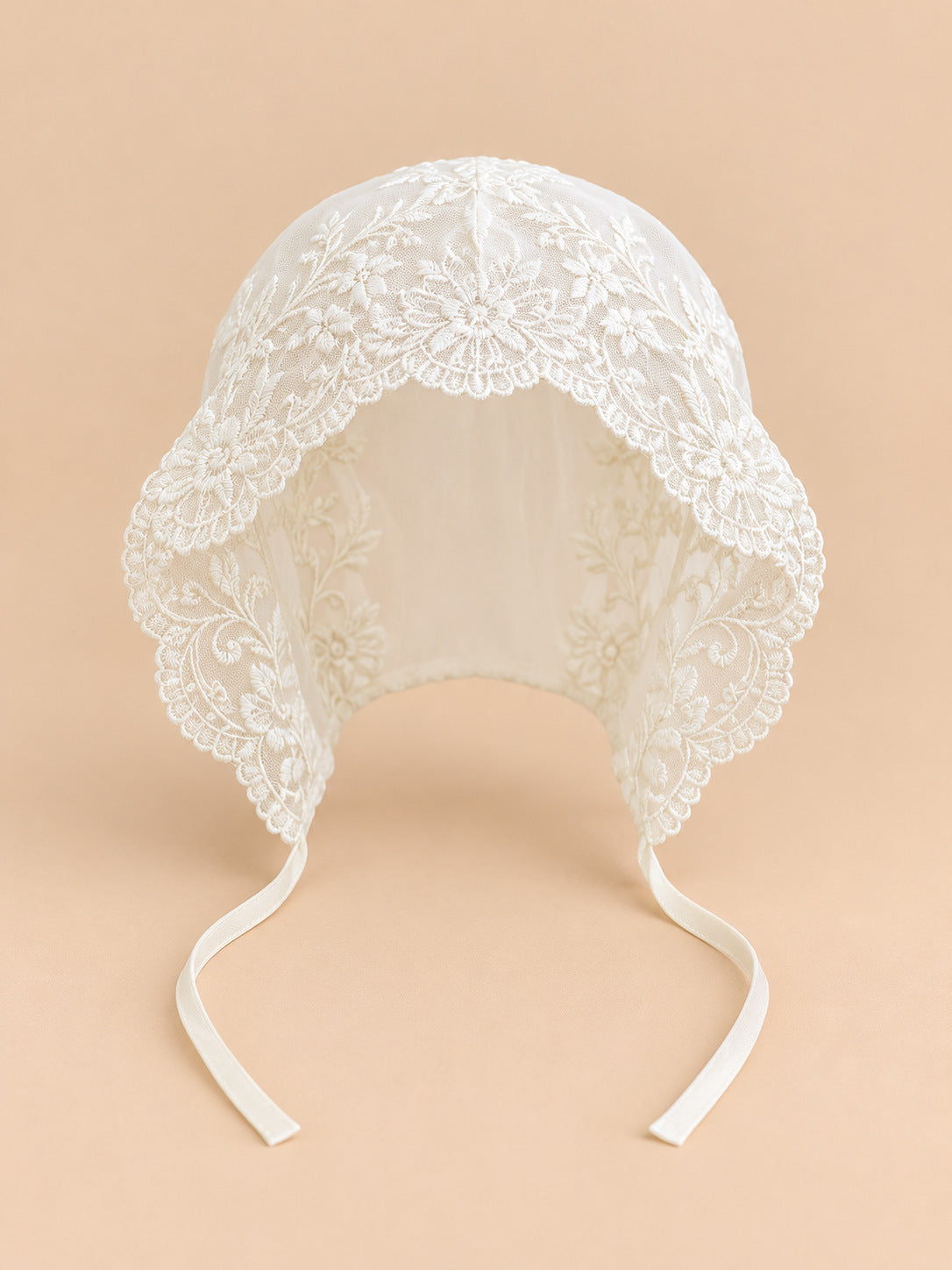 Béguin bébé fille en dentelle brodée, modèle 01, vue de face sur fond pêche sable