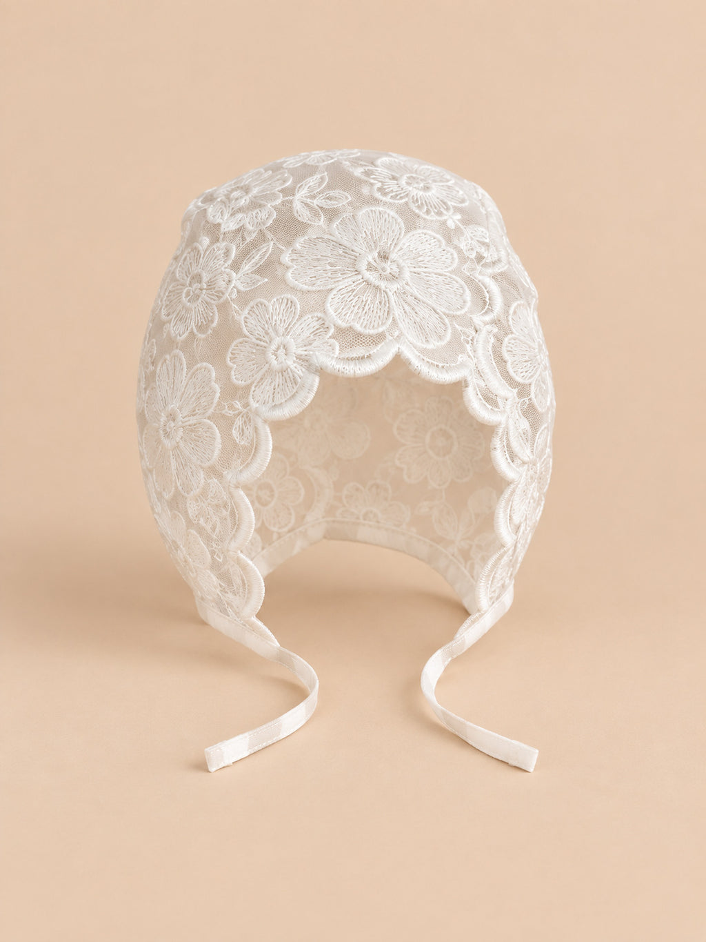 Béguin bébé fille en dentelle brodée, modèle 12, vue de face sur fond pêche sable