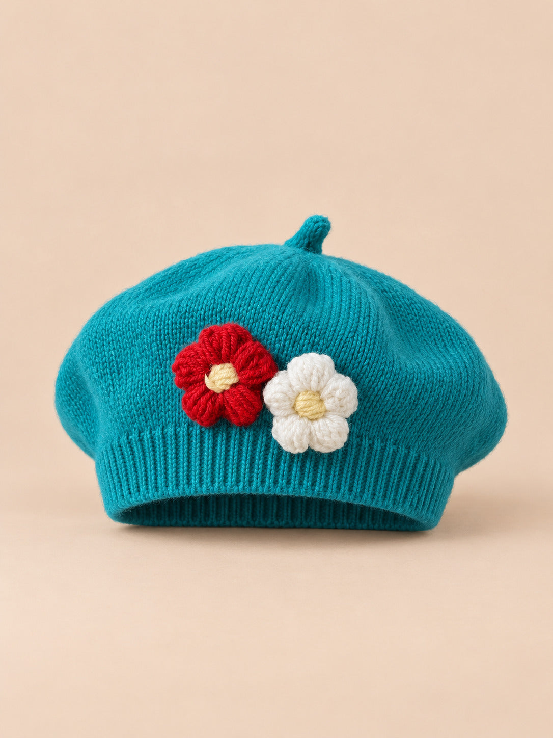 Béret bébé fille Bleu roi à fleurs en relief au crochet, vue de face sur fond pêche sable