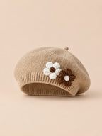 Béret bébé fille Café à fleurs en relief au crochet, vue de face sur fond pêche sable