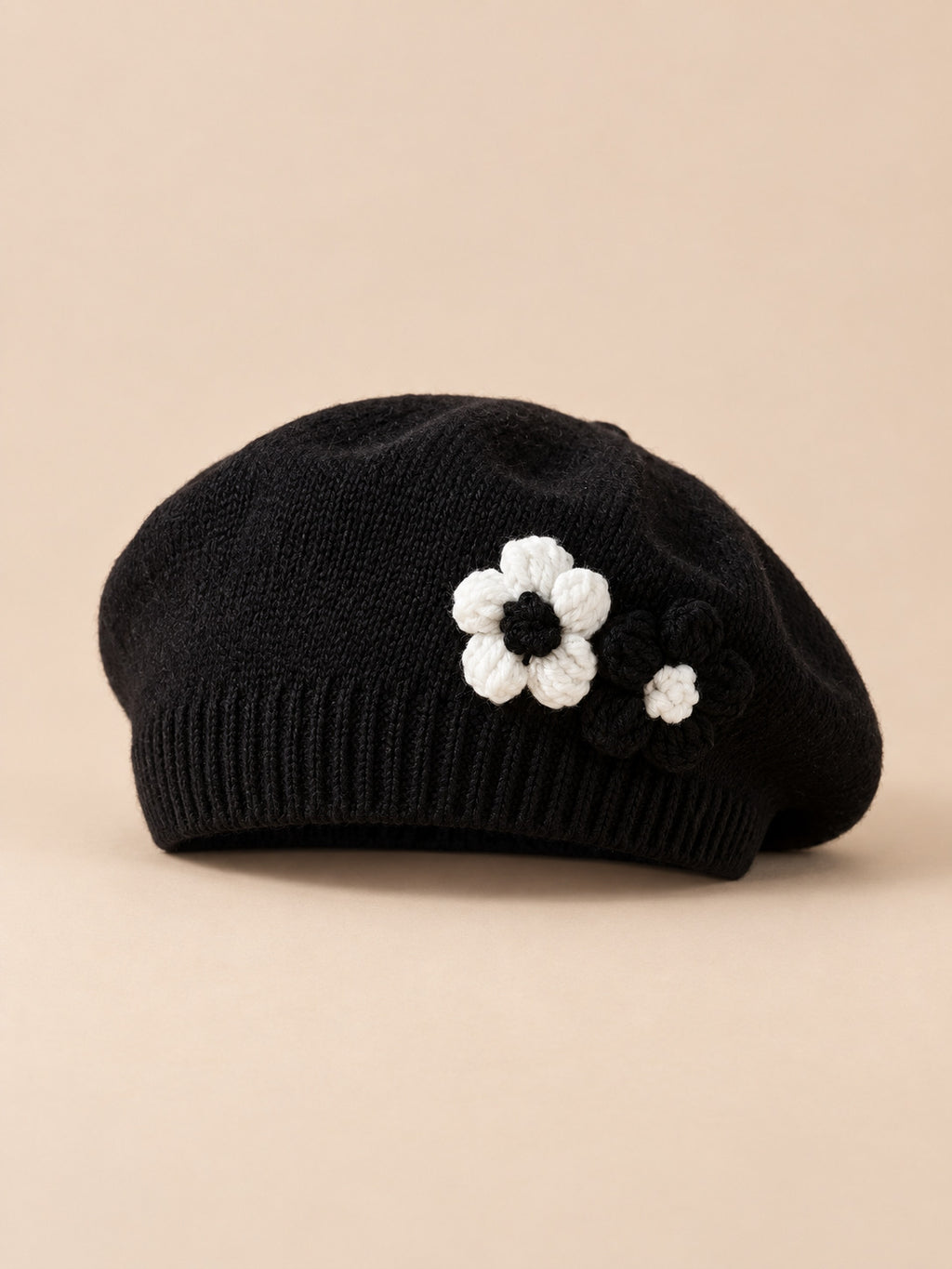 Béret bébé fille Noir à fleurs en relief au crochet, vue de face sur fond pêche sable