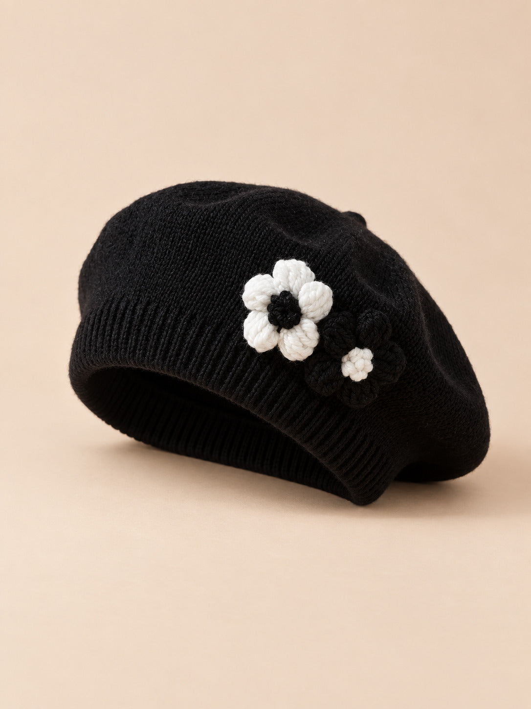 Béret bébé fille Noir à fleurs en relief au crochet, vue de trois quarts sur fond pêche sable