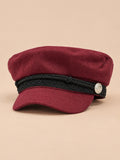 Gorra marinera de ocho paneles, estilo capitán, color burdeos, vista frontal, sobre fondo color arena y melocotón
