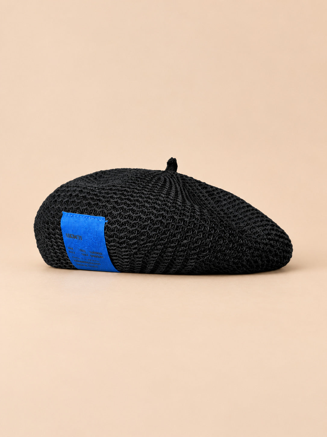 Béret d’été en lin ajouré noir, vue de face sur fond pêche sable