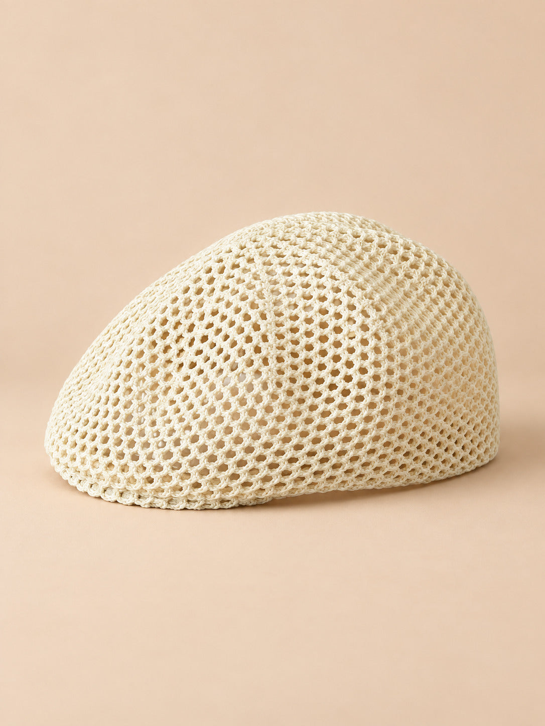 Béret résille ajouré blanc lait, vue de face sur fond pêche sable