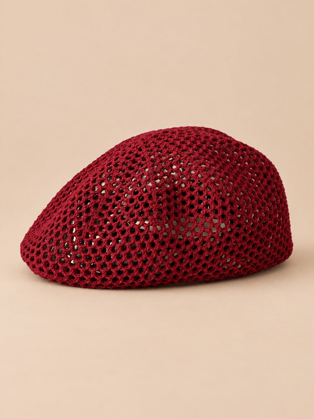 Béret résille ajouré lie de-vin, vue de face sur fond pêche sable