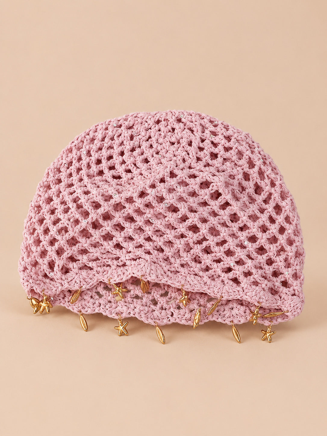 Béret rétro rose ajouré au crochet à franges d'étoiles dorées, vue de face sur fond pêche sable