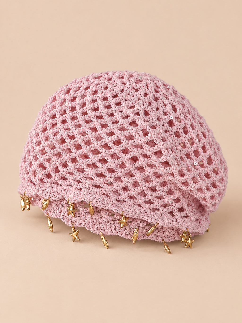 Béret rétro rose ajouré au crochet à franges d'étoiles dorées, vue trois quarts sur fond pêche sable