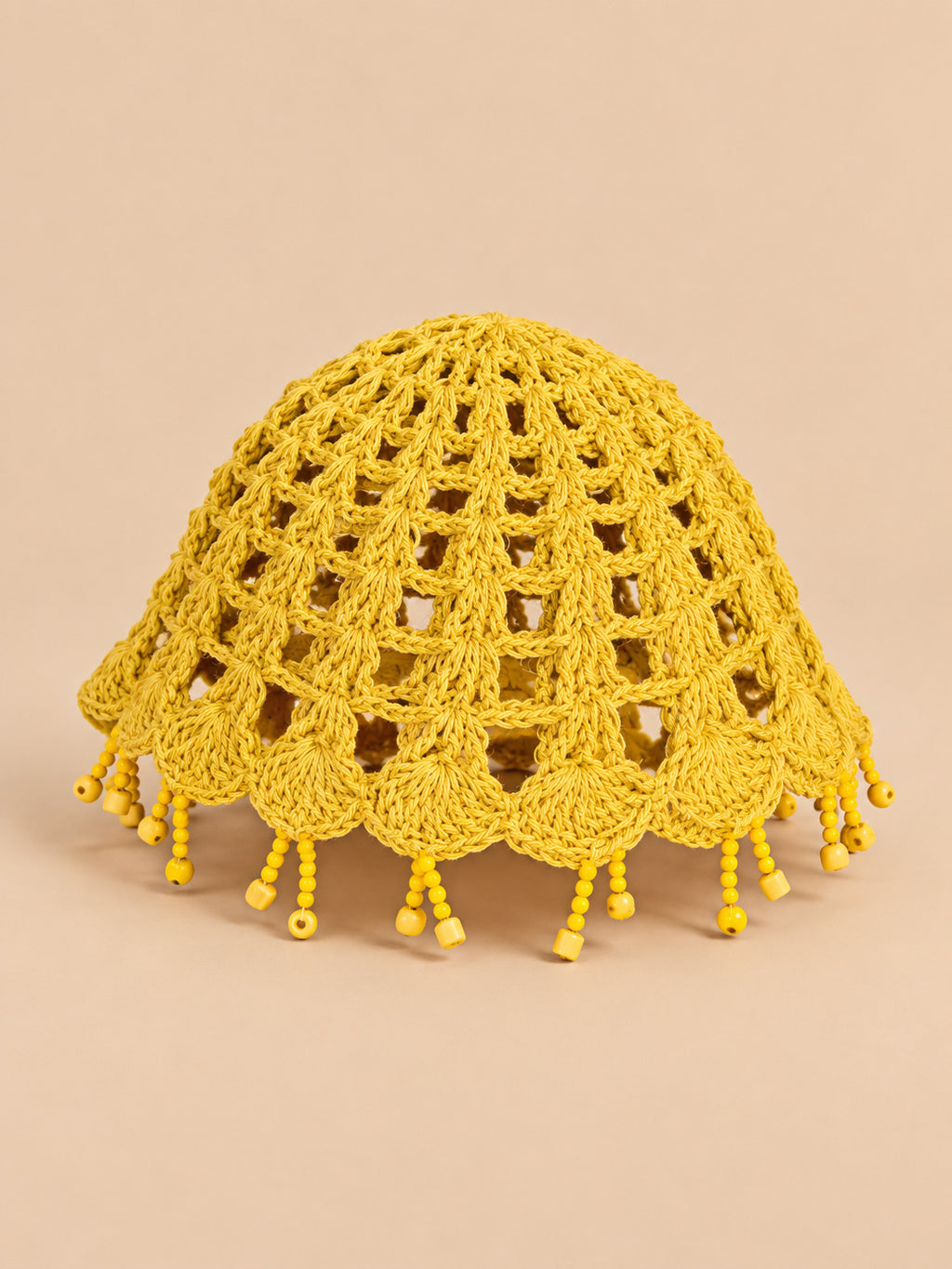 Béret crochet rétro jaune ajouré à franges de perles, vue trois quarts sur fond pêche sable