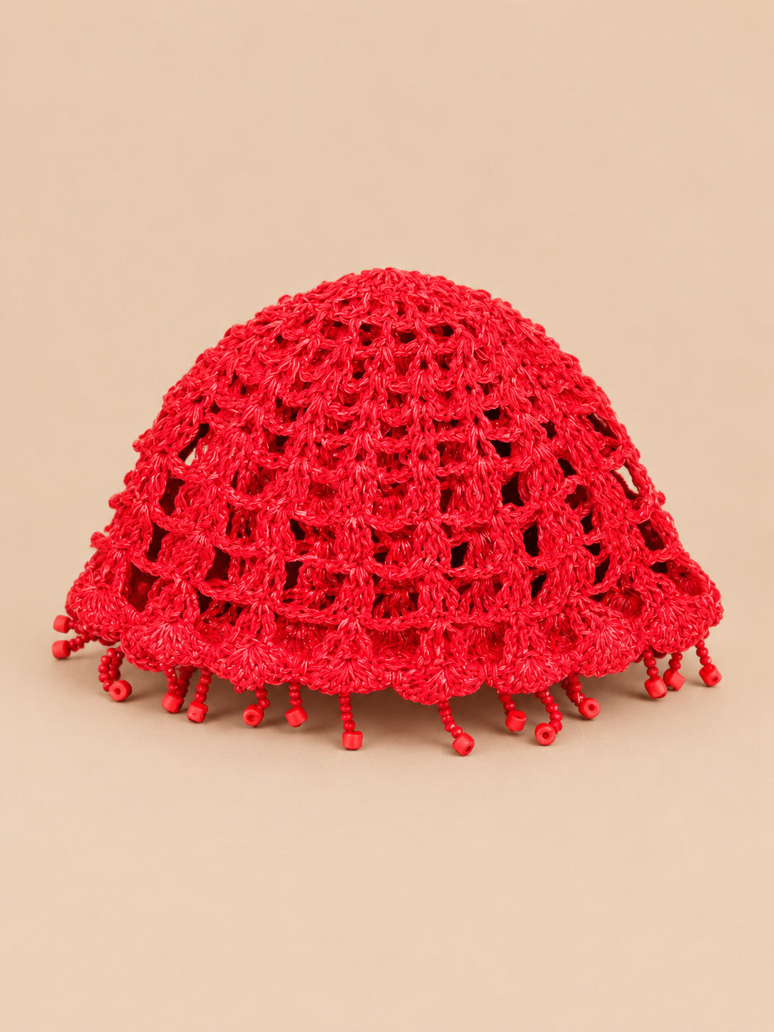 Béret crochet rétro rouge ajouré à franges de perles, vue de face sur fond pêche sable