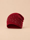 Gorro burdeos de mujer de punto con pedrería, de estilo streetwear, sobre fondo arena y melocotón