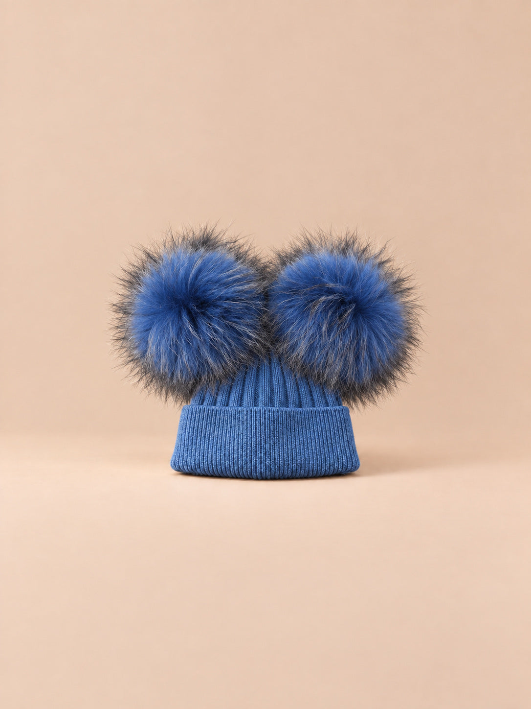 Bonnet double pompon, bleu, pompons assortis, vue de face sur fond pêche sable.