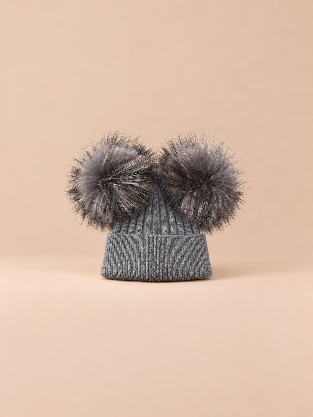 Bonnet double pompon, gris foncé, pompons assortis, vue de face sur fond pêche sable.