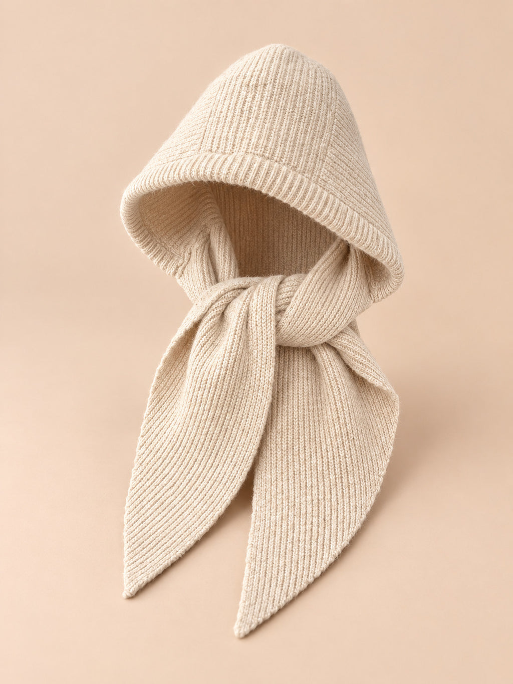 Cagoule bonnet-écharpe beige en maille, vue de trois quarts sur fond pêche sable