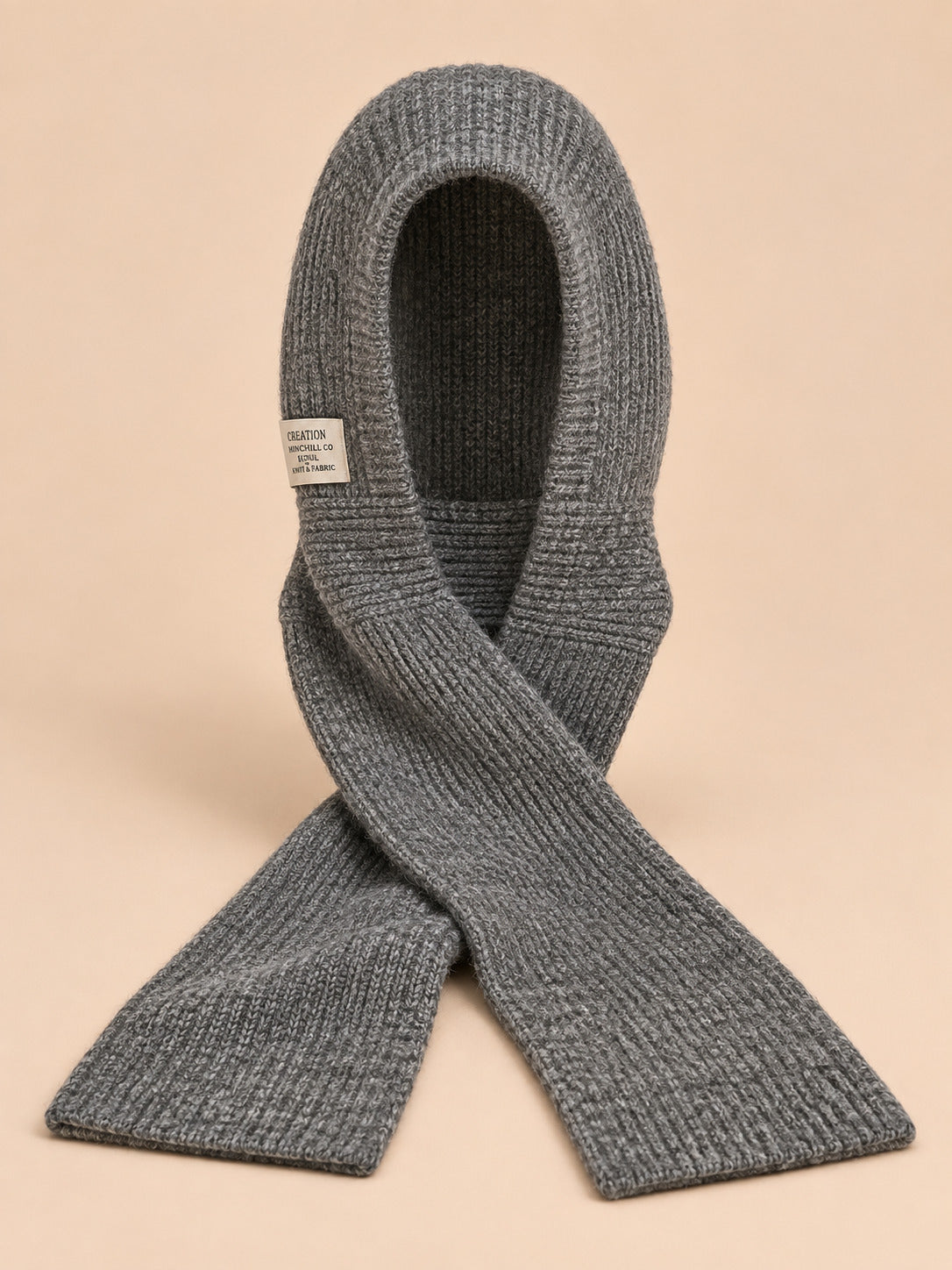 Cagoule bonnet-écharpe gris en maille, vue de face sur fond pêche sable