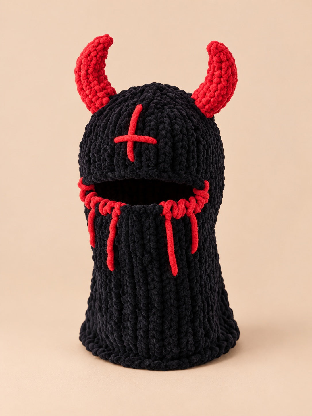 Cagoule crochet cornes de diable modèle 3 noire et rouge, vue de face sur fond pêche sable