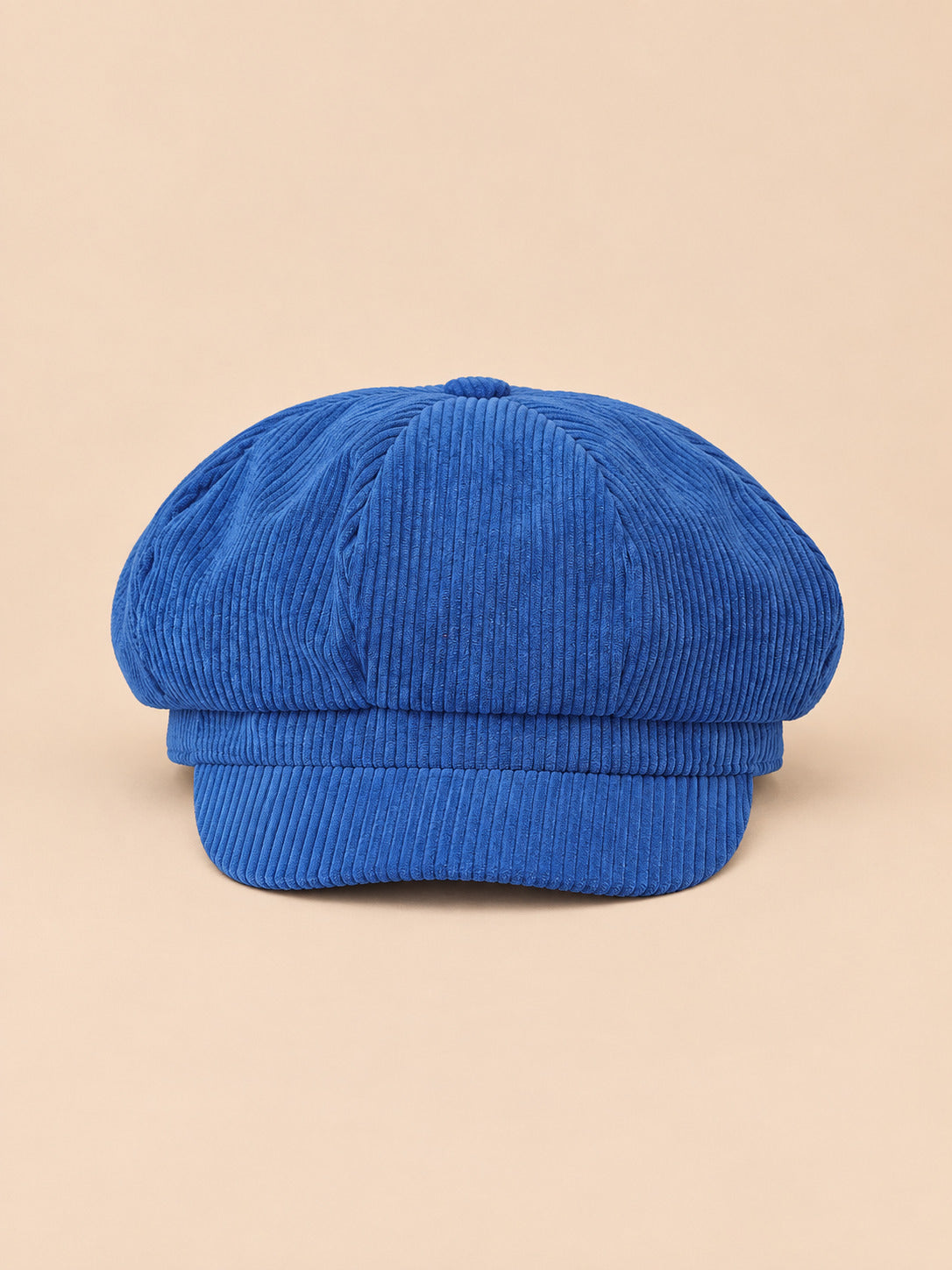 Casquette gavroche octogonale en velours côtelé bleu, vue de face sur fond pêche sable