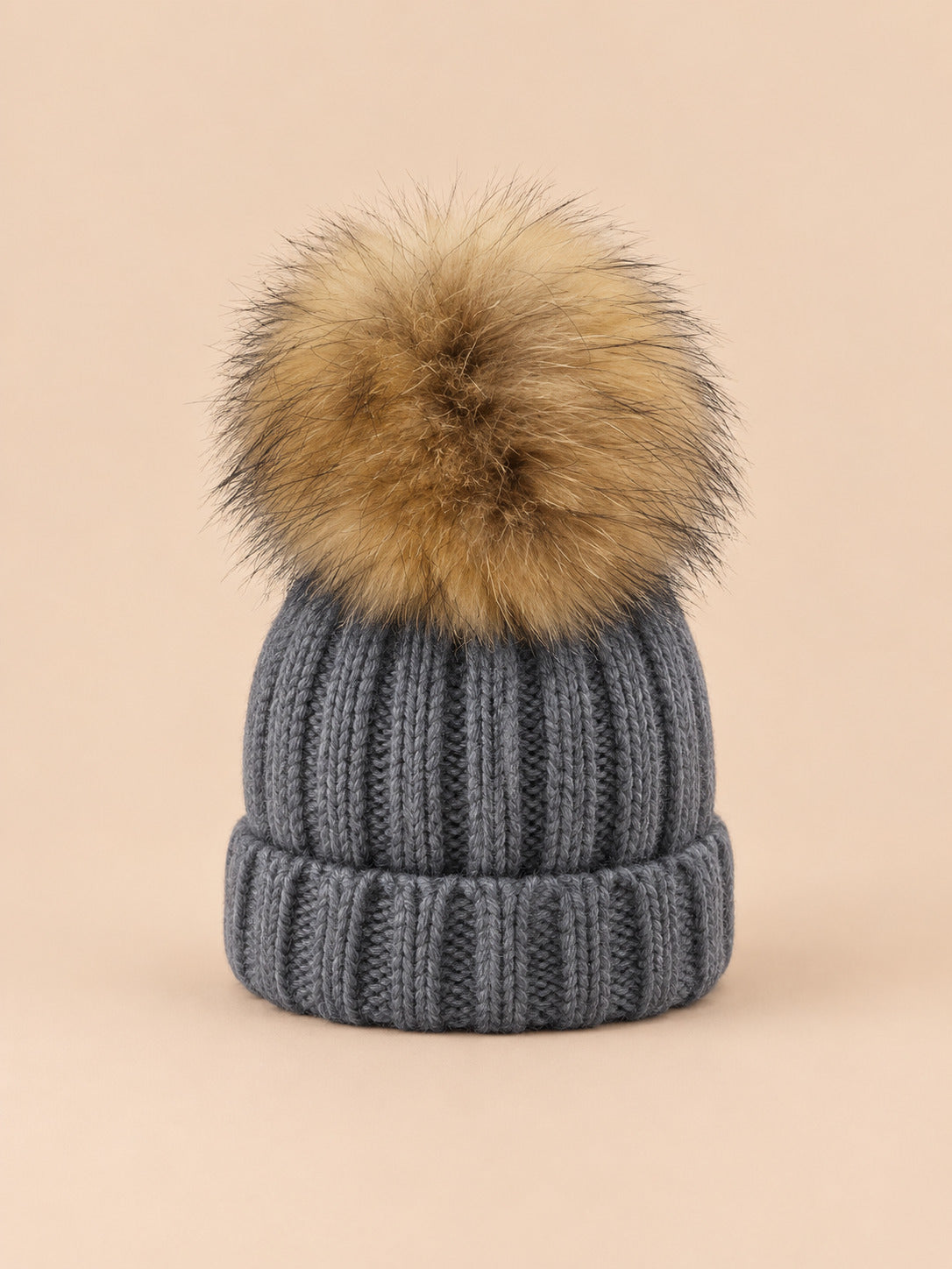 Bonnet enfant à pompon gris, vue de face sur fond pêche sable