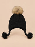 Bonnet enfant à pompon noir torsade, vue de face sur fond pêche sable