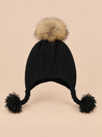 Bonnet enfant à pompon noir torsade, vue de face sur fond pêche sable