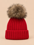 Gorro rojo infantil con pompón, parte del conjunto de gorro y bufanda, sobre fondo arena y melocotón