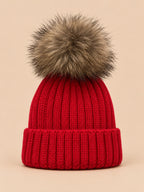 Gorro rojo infantil con pompón, parte del conjunto de gorro y bufanda, sobre fondo arena y melocotón