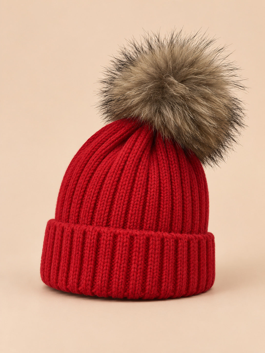 Bonnet enfant à pompon rouge, vue de trois quarts sur fond pêche sable