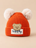Gorro infantil con osito y dos pompones, color naranja, vista frontal en la fotografía del producto