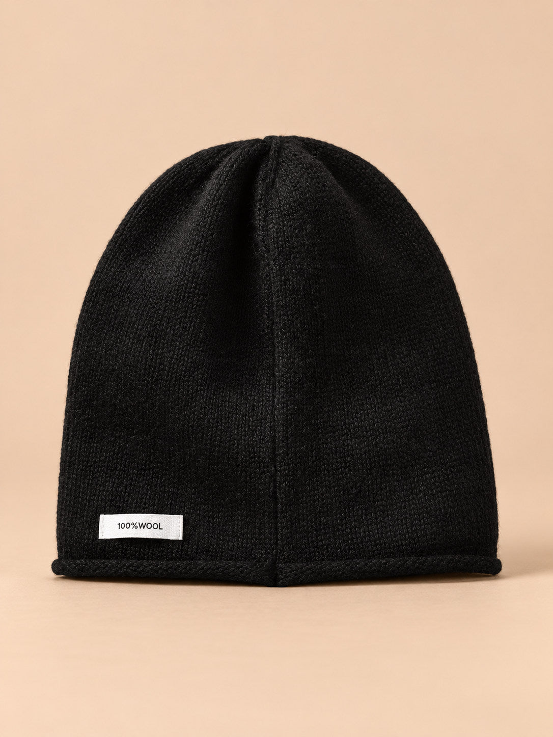 Bonnet femme en pure laine noir, vue de face, fond pêche sable