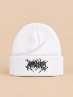 Bonnet en maille chaud blanc à broderie noire, vue de face sur fond pêche sable