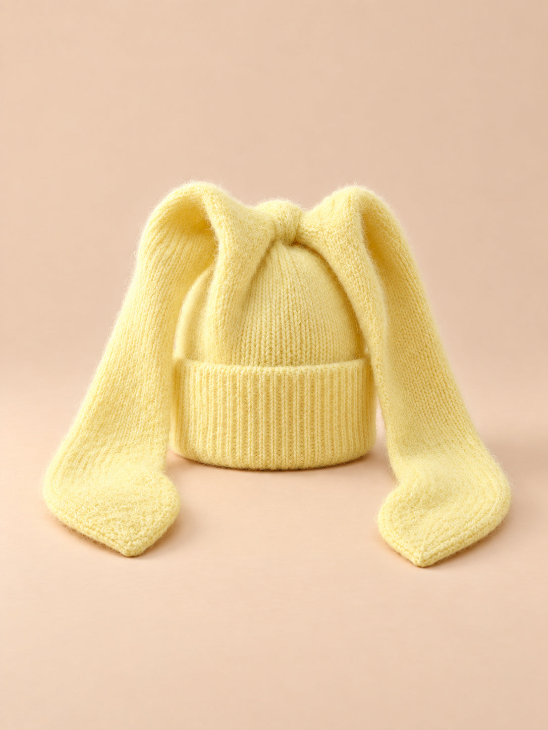 Bonnet à oreilles de lapin, jaune, vue de face sur fond pêche sable.