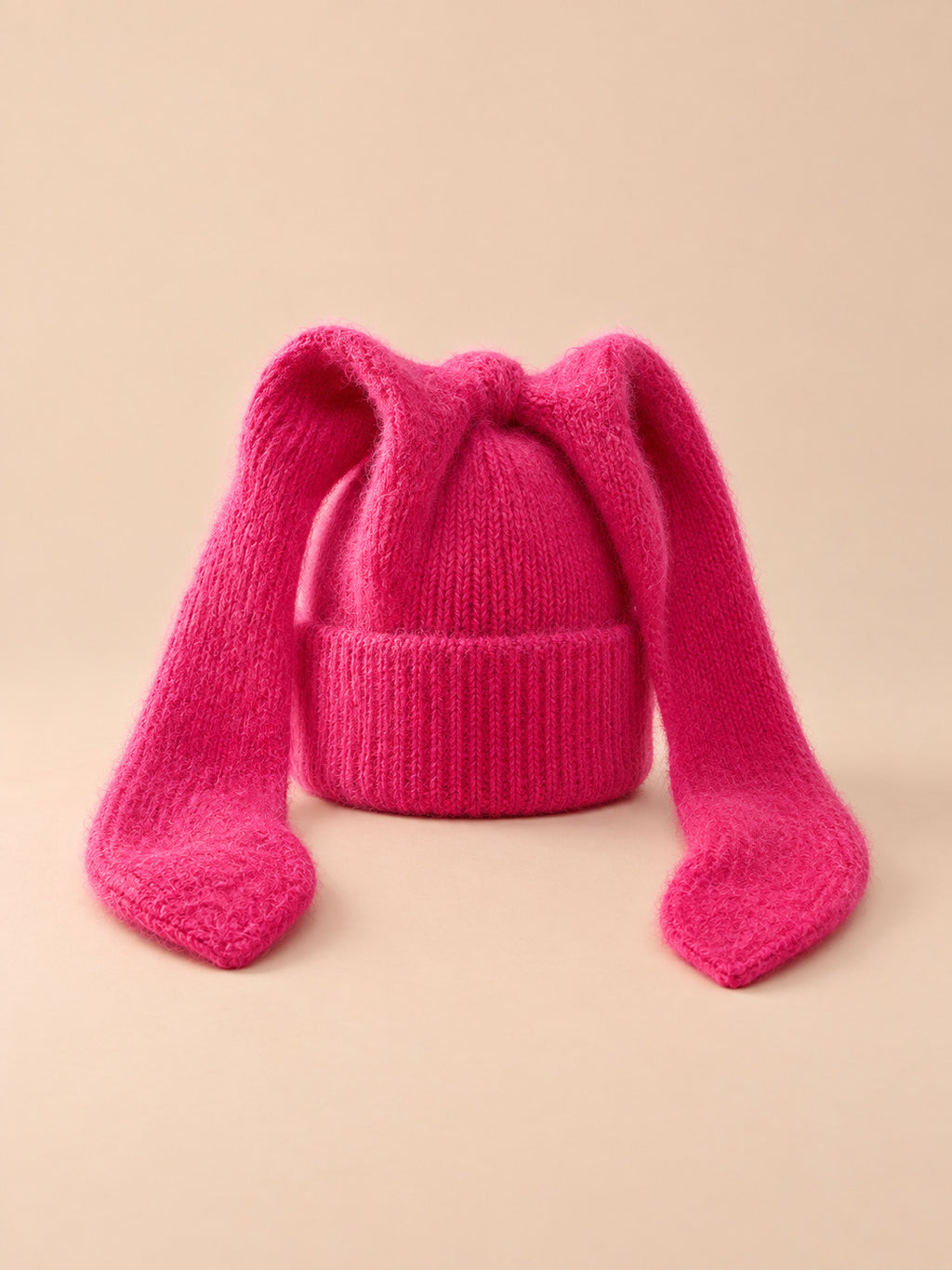 Gorro rojo de mujer de ganchillo acrílico con orejas de conejo, fotografiado sobre fondo arena y melocotón