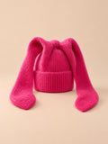 Gorro rojo de mujer de ganchillo acrílico con orejas de conejo, fotografiado sobre fondo arena y melocotón