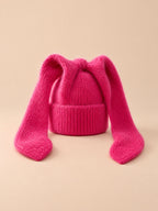 Gorro rojo de mujer de ganchillo acrílico con orejas de conejo, fotografiado sobre fondo arena y melocotón