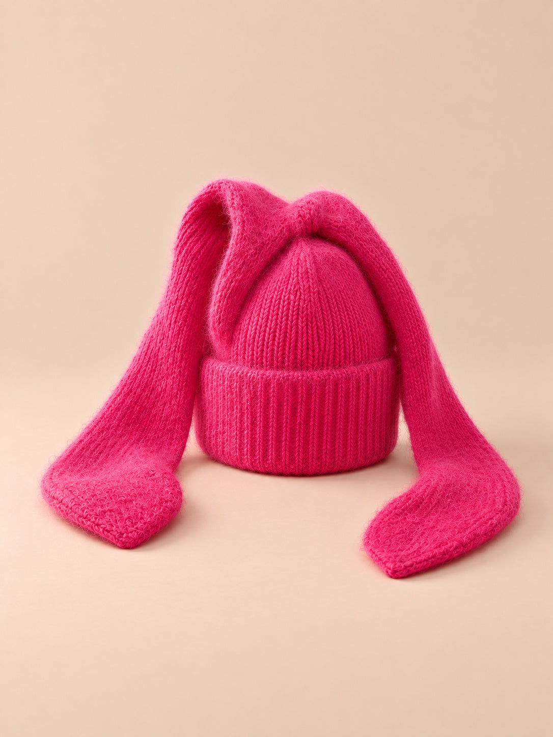 Bonnet femme à longues oreilles de lapin rouge fuchsia, vue de trois quarts sur fond pêche sable.
