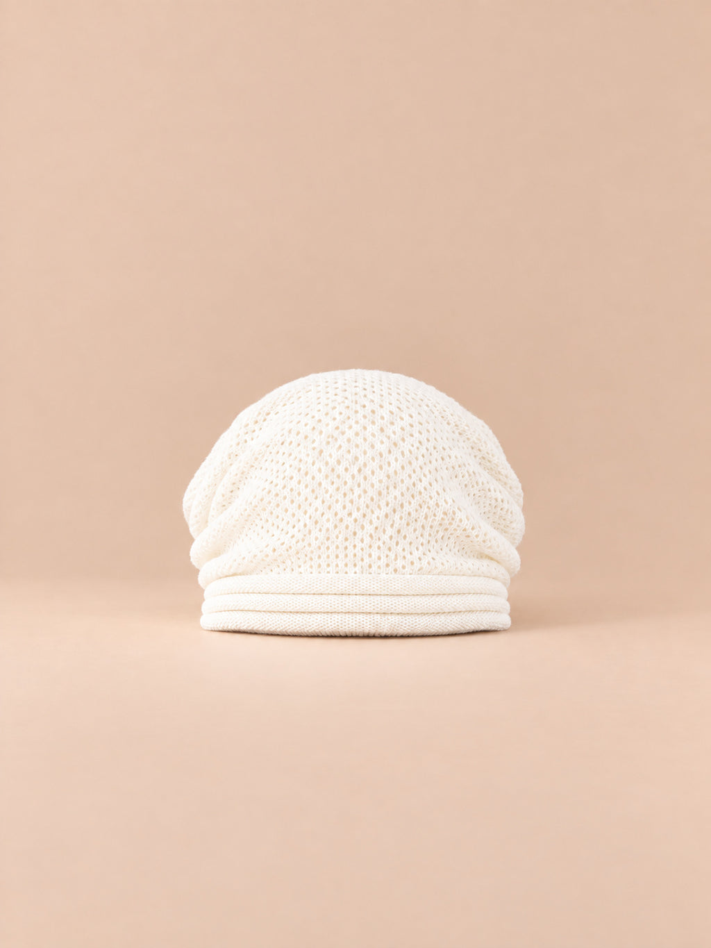 Bonnet oversize en maille blanc, vue de face sur fond pêche sable.