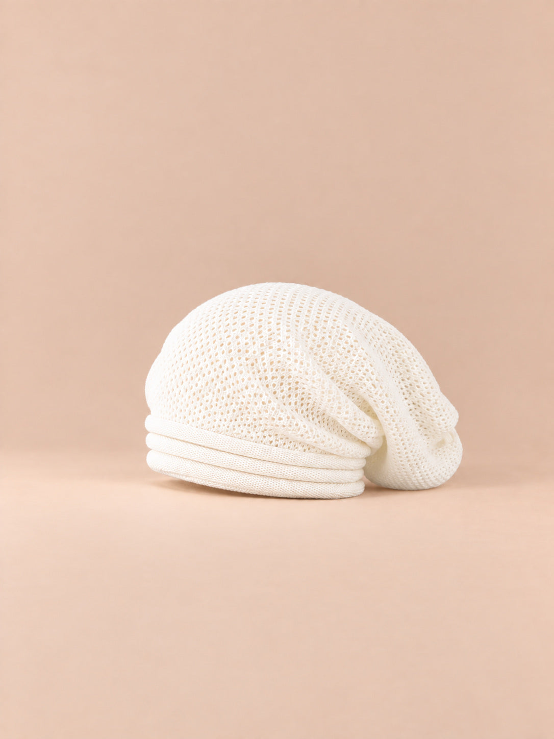 Bonnet oversize en maille blanc, vue de trois quarts sur fond pêche sable.