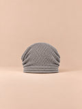 Bonnet oversize en maille gris clair, vue de face sur fond pêche sable.