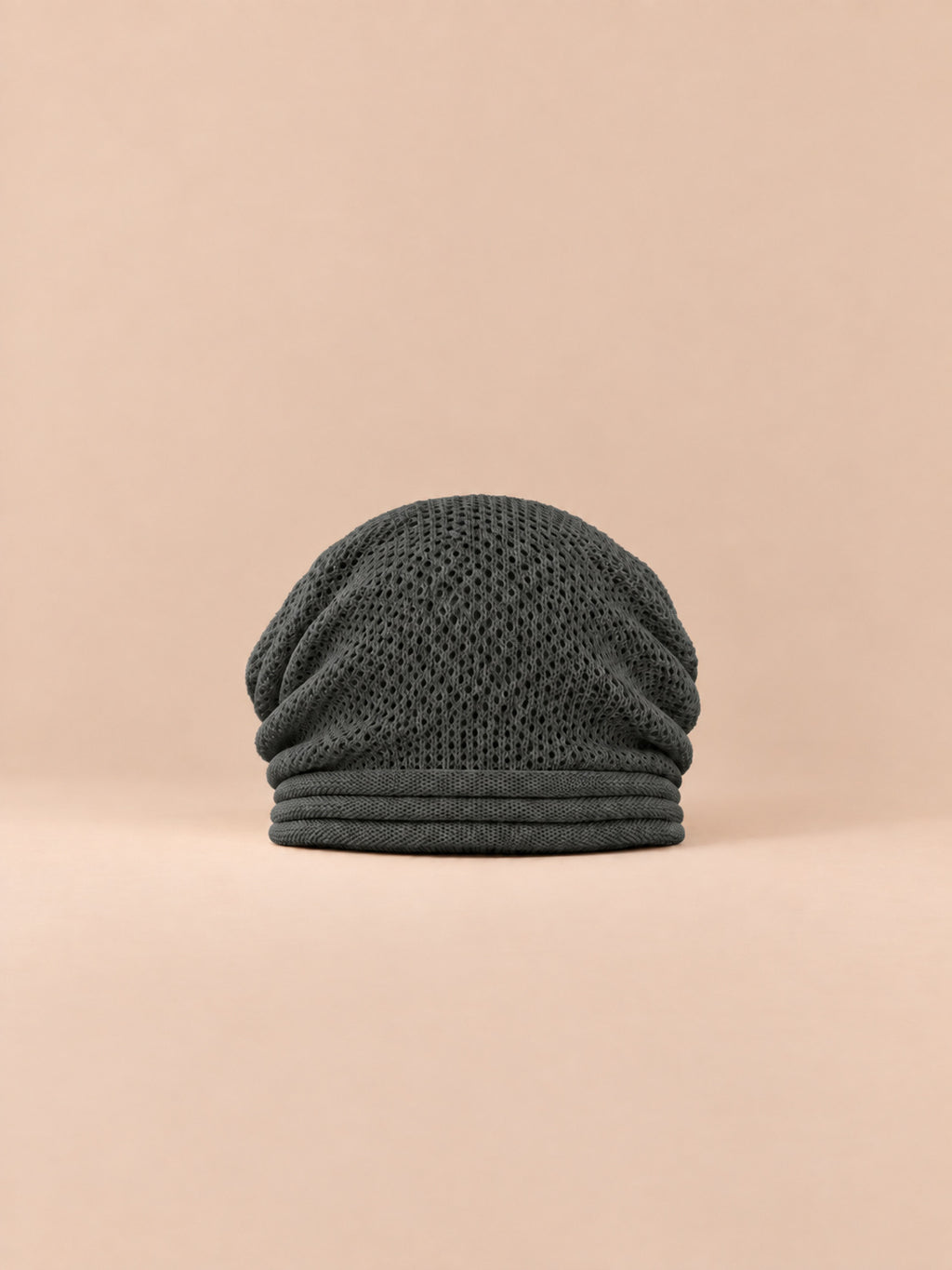 Gorro oversize de punto cálido y cortavientos, color gris oscuro, vista frontal, sobre fondo color arena y melocotón
