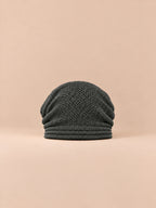Gorro oversize de punto cálido y cortavientos, color gris oscuro, vista frontal, sobre fondo color arena y melocotón