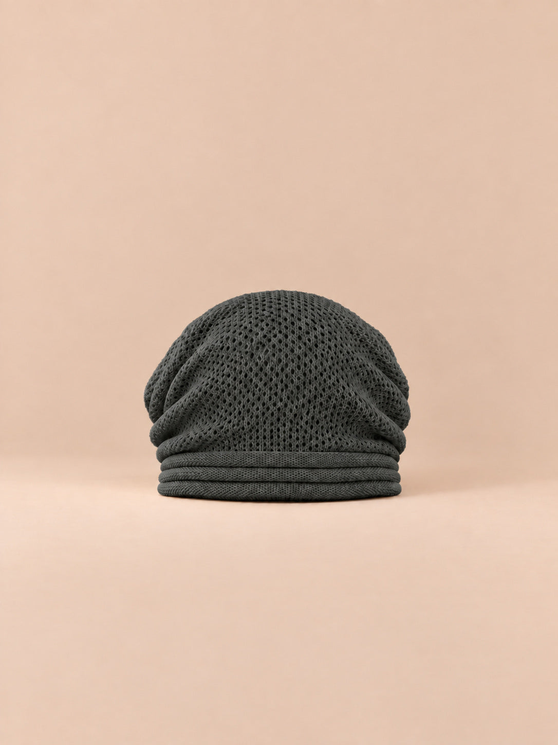 Bonnet oversize en maille gris foncé, vue de face sur fond pêche sable.