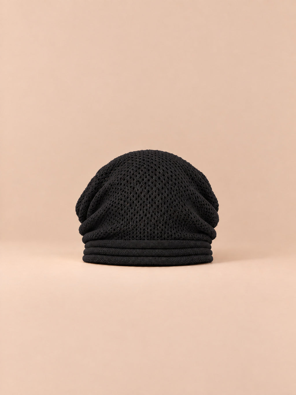Gorro oversize de punto cálido y cortavientos, color negro, vista frontal, sobre fondo color arena y melocotón