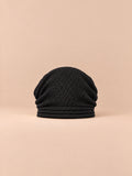 Gorro oversize de punto cálido y cortavientos, color negro, vista frontal, sobre fondo color arena y melocotón