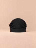 Gorro oversize de punto cálido y cortavientos, color negro, vista frontal, sobre fondo color arena y melocotón