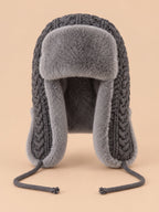 Gorro peruano de mujer con orejeras y cintas, color gris, vista frontal, sobre fondo color arena y melocotón
