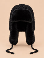 Gorro peruano de mujer con orejeras y cintas, color negro, vista frontal, sobre fondo color arena y melocotón