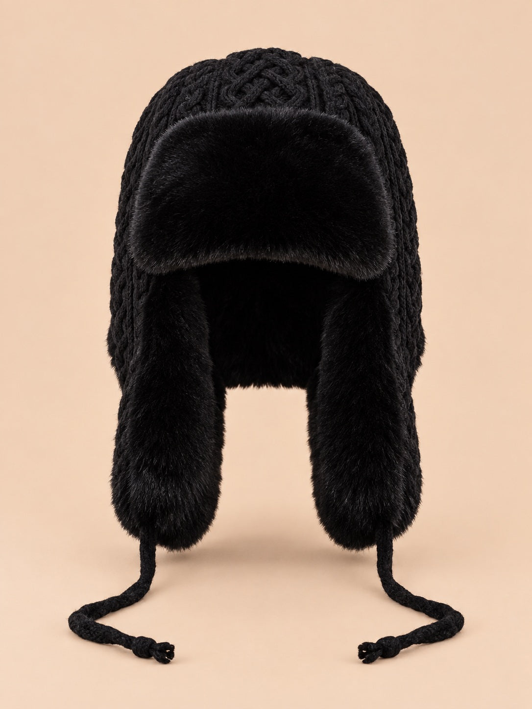 Gorro peruano de mujer con orejeras y cintas, color negro, vista frontal, sobre fondo color arena y melocotón