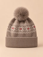 Gorro de cachemira color camel con pompón y orejeras, fotografiado sobre fondo arena y melocotón