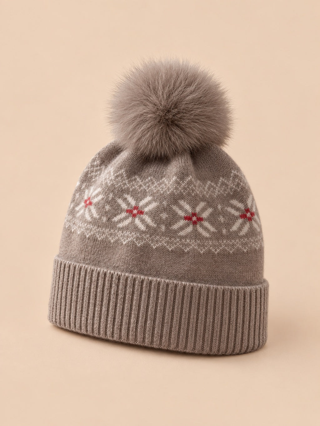 Bonnet cachemire camel à pompon et motif nordique, vue trois quarts sur fond pêche sable